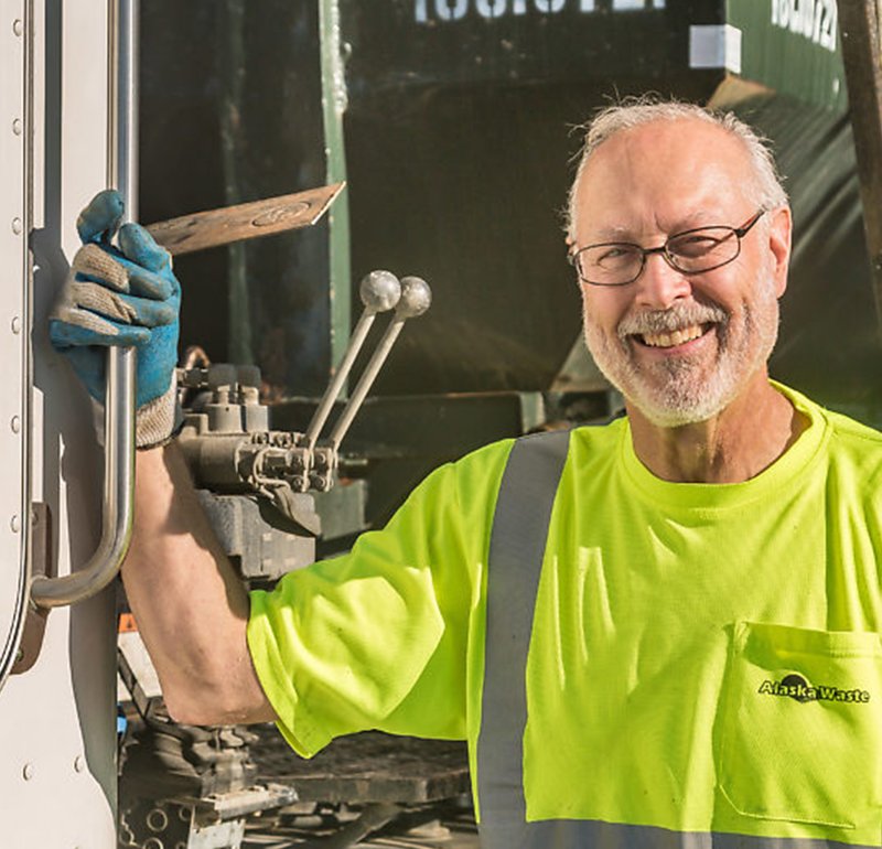 Alaska Waste Professional Driver smiling by his truck.
