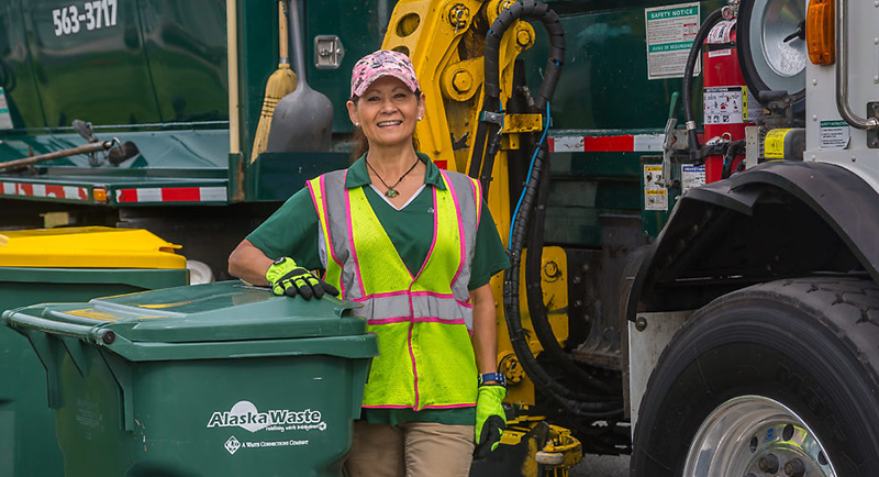 Photo of Alaska Waste employee standing between a truck and a bin.